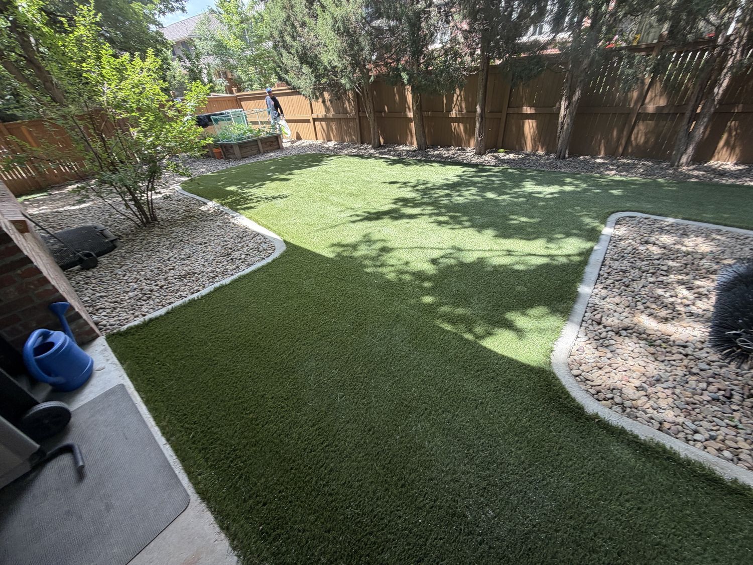 Backyard with freshly installed green artificial turf, gravel border and wooden fence