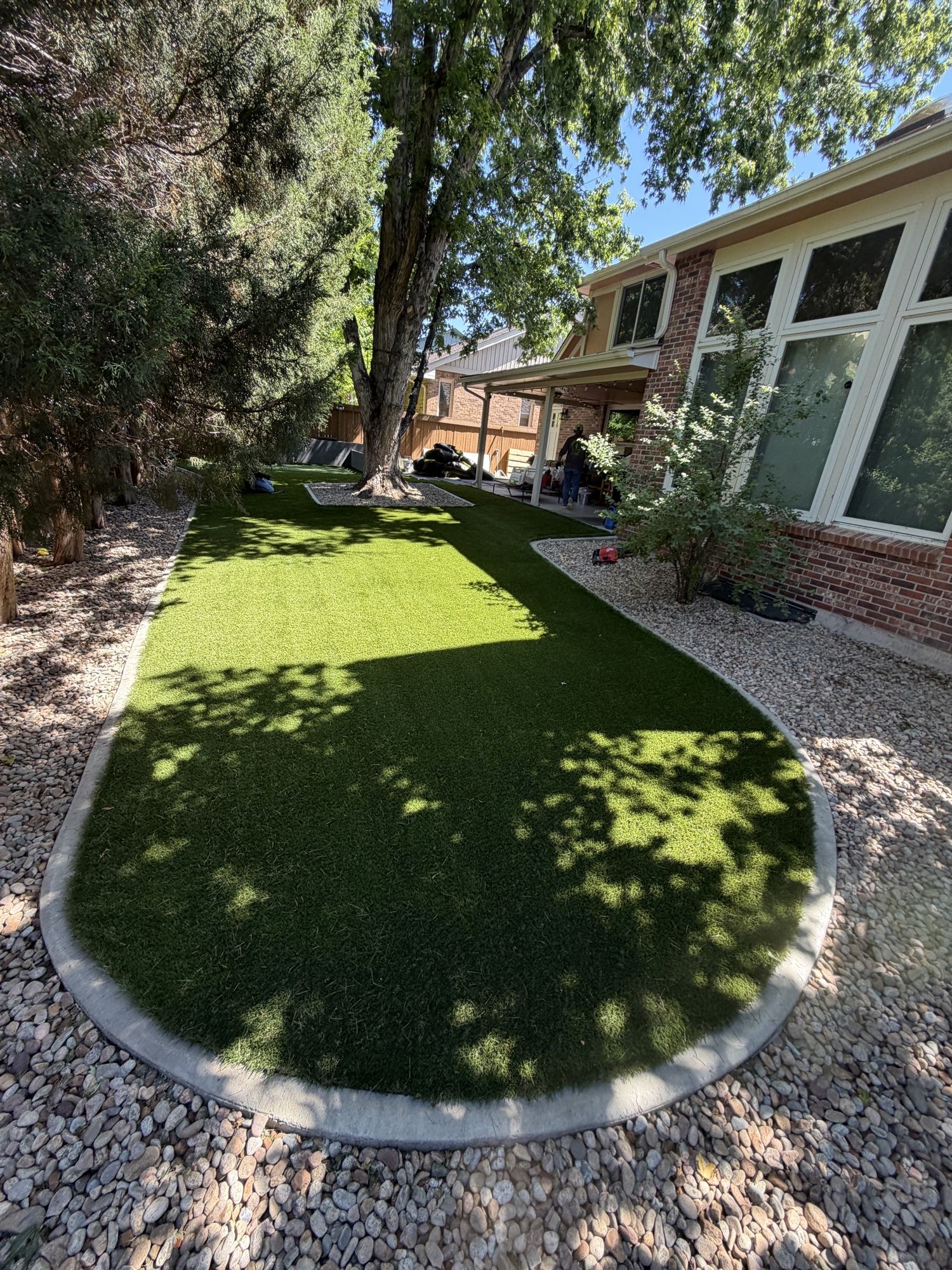 Landscaped backyard with rectangular artificial turf surrounded by gravel, trees and house