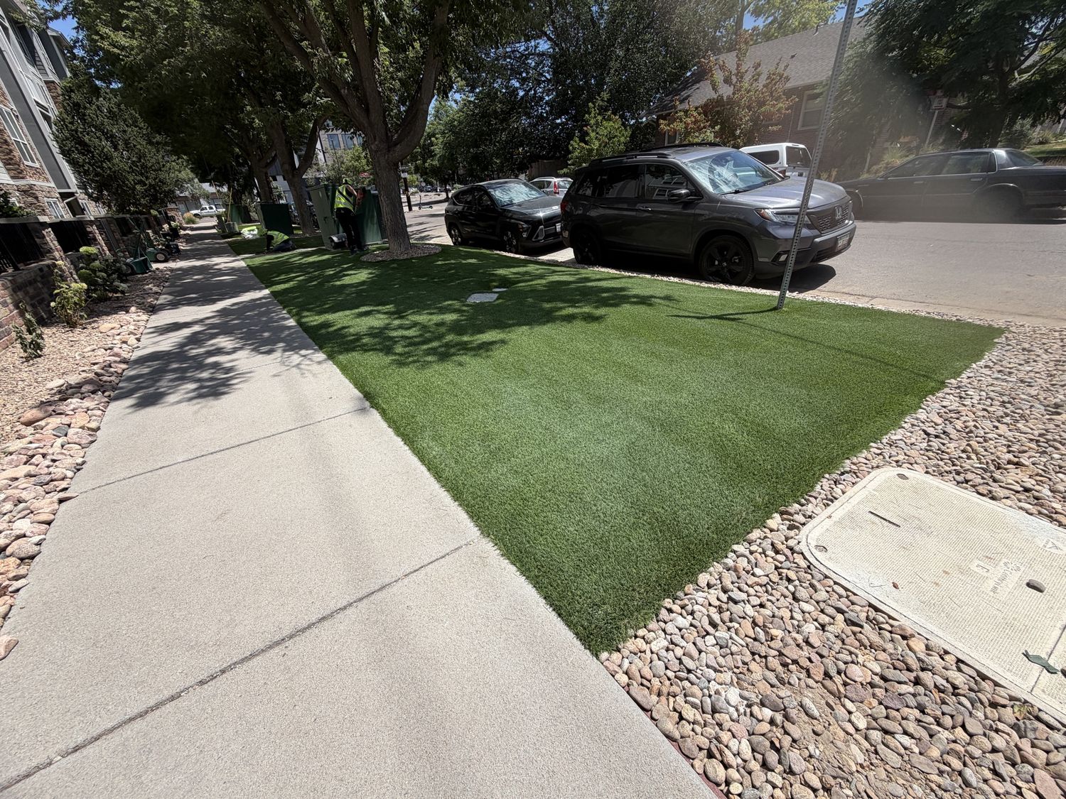 Wide view of a sidewalk next to a large manicured artificial turf area on a residential street
