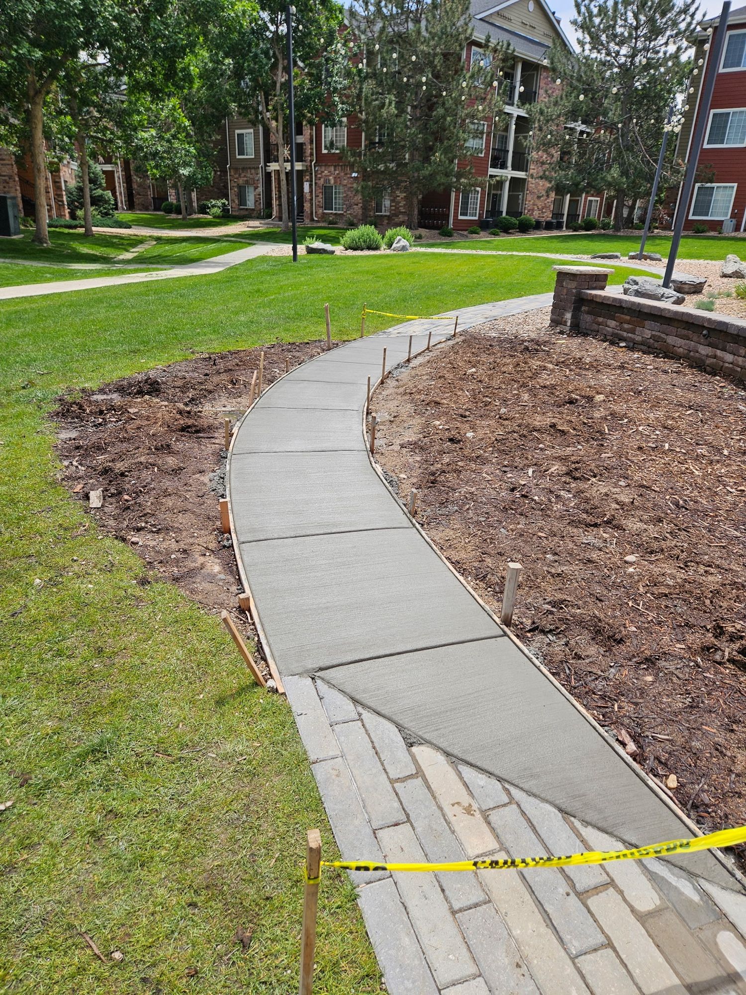 Newly poured curving concrete walkway between a lawn and mulched garden bed