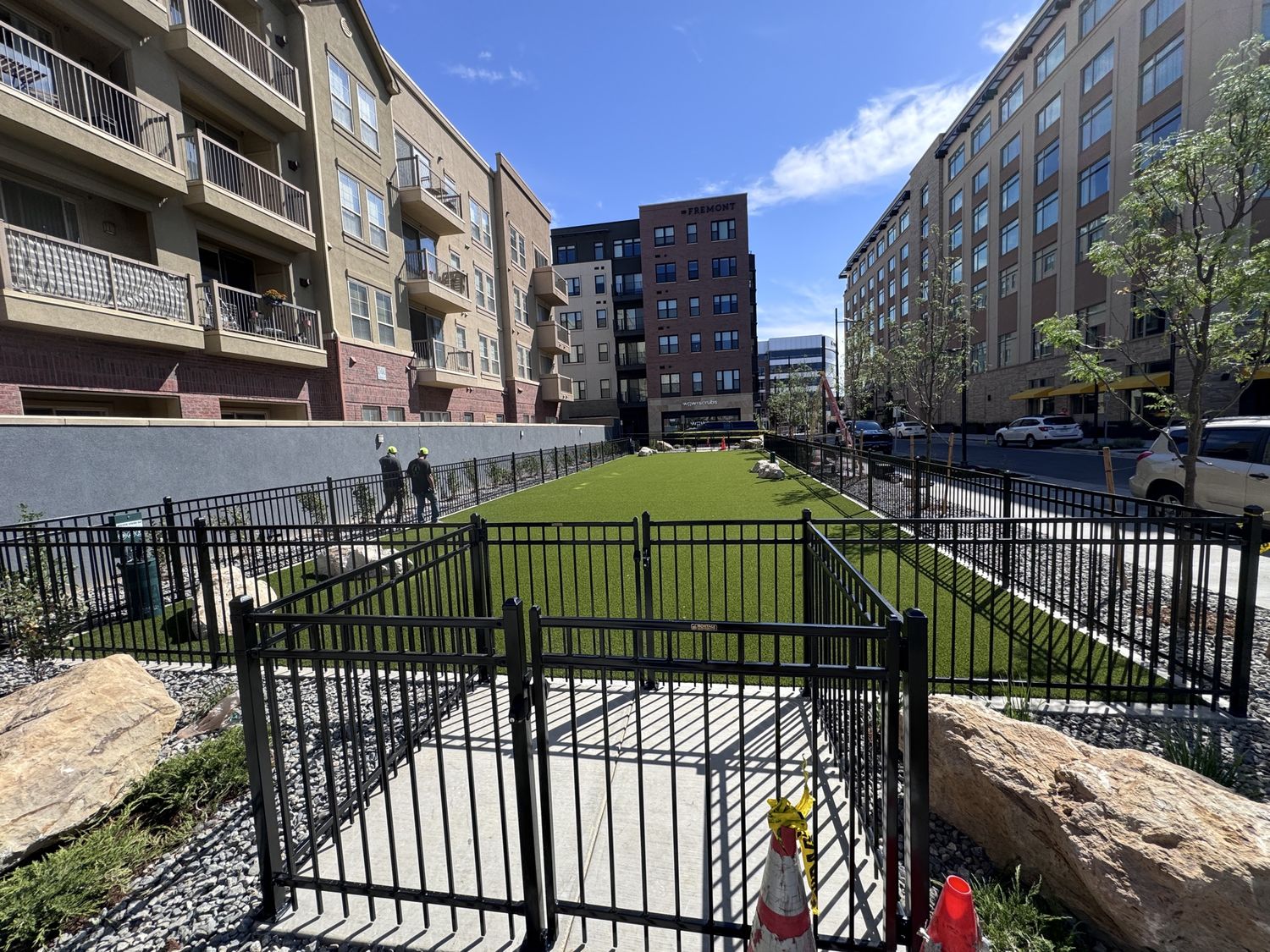 Black metal gated entrance to a park area with concrete paths and turf