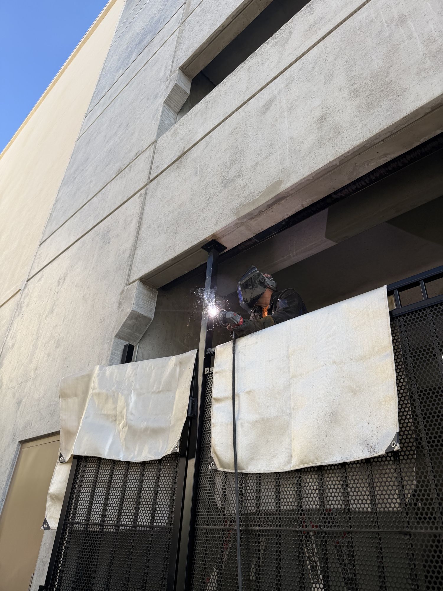Close-up of welding repair work on a black metal gate with protective cloths draped