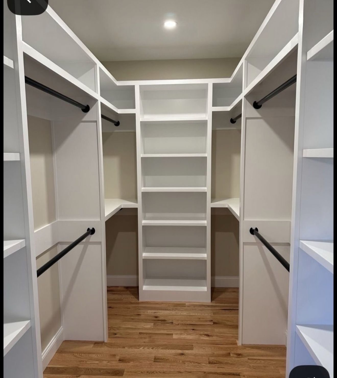 Walk-in closet with custom white shelving, cubbies and hanging rods over light wood floor